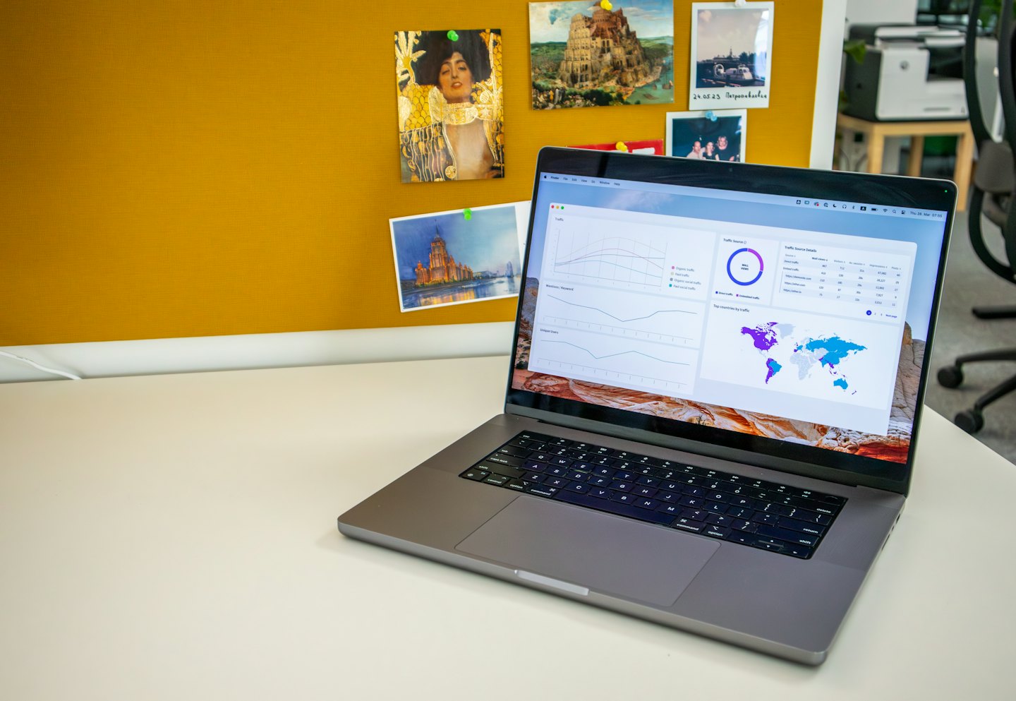 Notebook s grafy na bílém stole se žlutou nástěnkou.